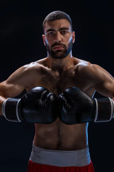 Portrait of tough male boxer posing in boxing stance against black background.
