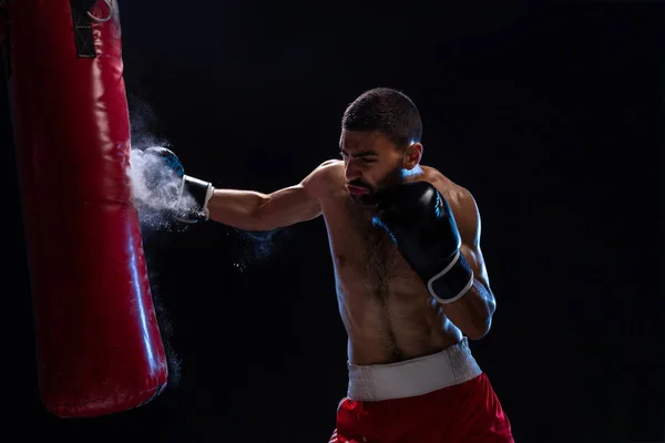 Boxeador musculoso guapo dando una patada hacia adelante contundente durante una ronda de práctica con una bolsa de boxeo . — Foto de Stock