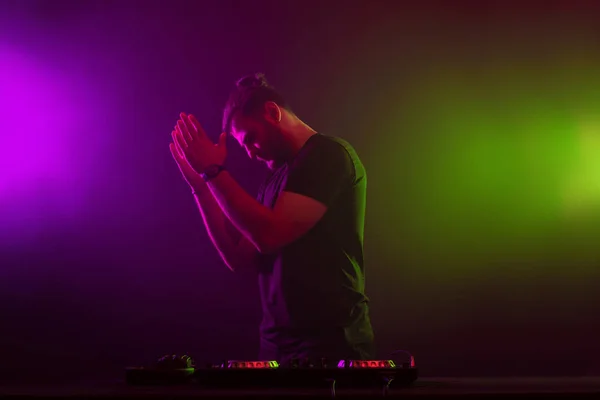 DJ at work mixing sound on her decks at a party or night club with colourful smoke light background