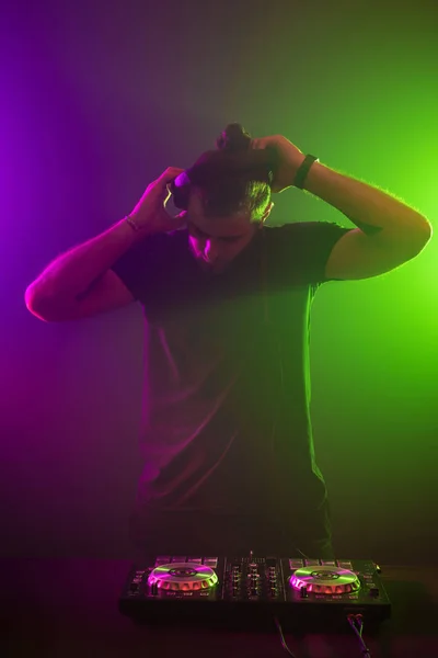 DJ no trabalho misturando som em seus conveses em uma festa ou clube noturno com fundo colorido fumaça luz — Fotografia de Stock