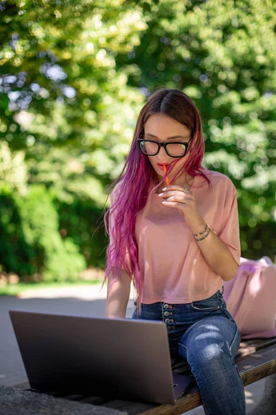 Молодая девушка учится в весеннем парке, сидит на деревянной скамейке и просматривает ноутбук — стоковое фото