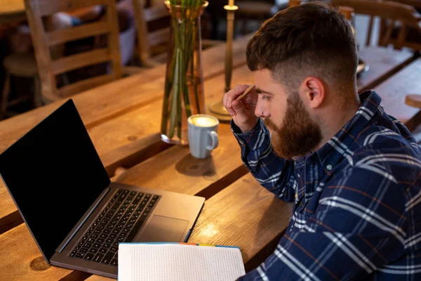 Hombre joven charlando a través de net-book durante el descanso de trabajo en la cafetería, hombre sentado en la computadora portátil abierta frontal con pantalla de espacio de copia en blanco . —  Fotos de Stock