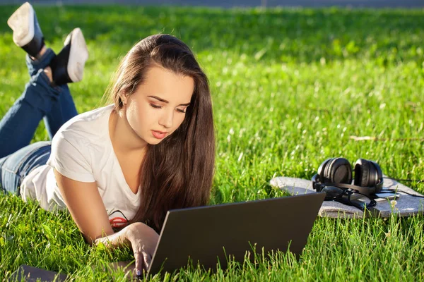 Giovane donna che utilizza il computer portatile nel parco sdraiato sull'erba verde. Tempo libero concetto di attività. — Foto Stock