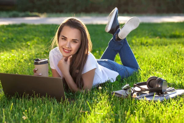 Mladá žena používající notebook v parku ležící na zelené trávě. Koncept volnočasové aktivity. — Stock fotografie