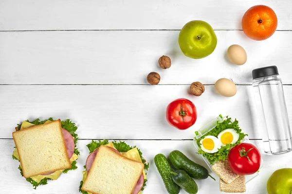 Öğle Yemeği. Sandviç ve taze sebze, şişe su, fındık ve meyve Beyaz ahşap zemin üzerinde. Sağlıklı beslenme kavramı. Kopya alanı ile üstten görünüm
