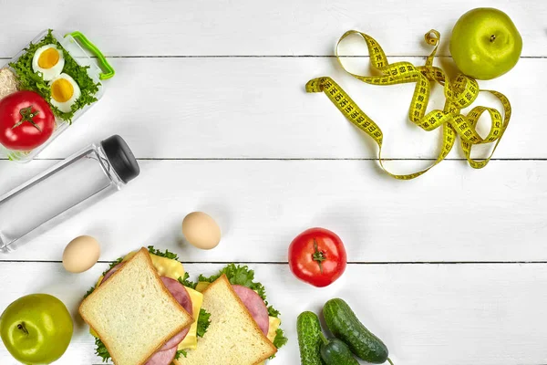 Lunch. Broodjes en verse groenten, fles water en groene appel op houten tafel. Gezond eten concept. Bovenaanzicht — Stockfoto