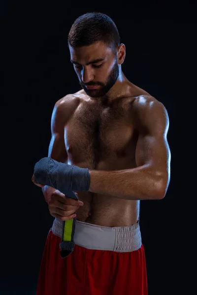 O boxeador de desporto puxa os envoltórios do pulso da mão. Oriental modelo masculino isolado no fundo preto . — Fotografia de Stock