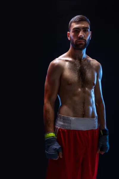 Joven boxeador masculino usando sus pantalones cortos de boxeo rojos y vendaje sobre fondo negro — Foto de Stock