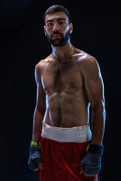 Boxeador listo para pelear. Boxeador con manos fuertes y puños apretados en tirantes azules sobre fondo negro — Foto de Stock