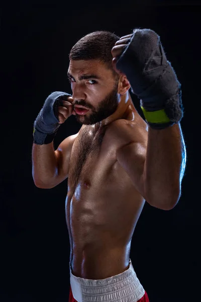 Boxing man ready to fight. Boxer with strong hands and clenched fists in blue straps against a black background