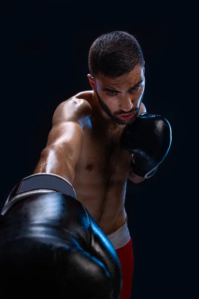 Mann schlägt auf Gegenspieler ein. fokussierter Kämpfer mit nacktem Oberkörper und Boxhandschuhen, der in die Kamera blickt. gewinnen. — Stockfoto