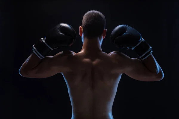 Vista trasera de un boxeador joven y fuerte. Modelo masculino Fitness con guantes de boxeo de pie sobre fondo negro . — Foto de Stock