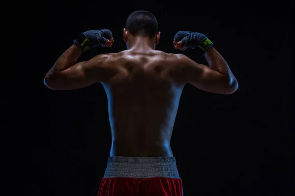 Vista trasera de un boxeador joven y fuerte. Modelo masculino Fitness con guantes de boxeo de pie sobre fondo negro . — Foto de Stock