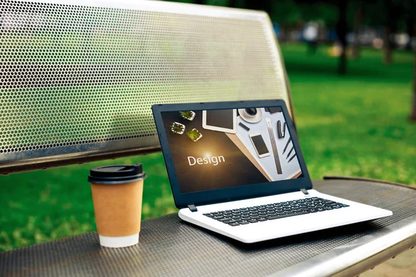 Laptop computer at the park background. Photo depicts notebook computer on the bench in the park, blurred green trees behind. Freelance concept.