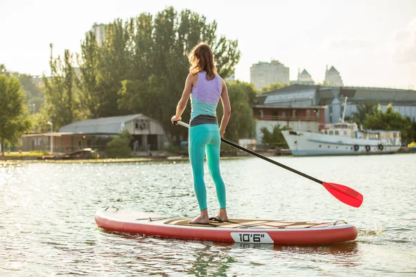 Frau schwebt an sonnigem Morgen auf einem Surfbrett. Stand Up Paddle Boarding - tolle aktive Erholung im Urlaub. — Stockfoto