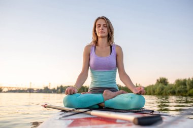 Genç güzel kadın Sup paddleboarding adlı bir denizde meditasyon. Sağlıklı yaşam tarzı.
