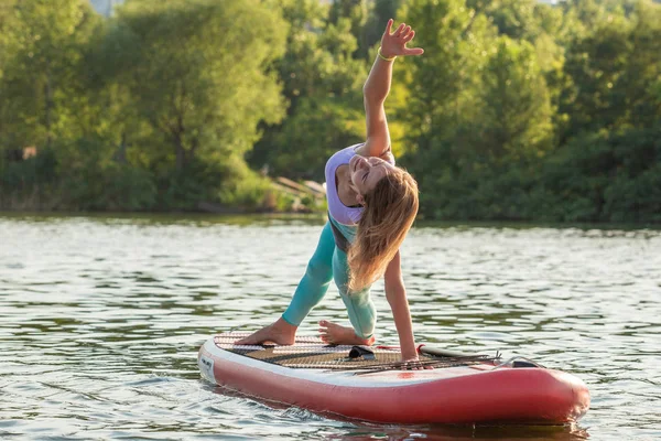 Ung kvinna gör yoga på sup bräda med paddel. Yogaställning, sidovy - begreppet harmoni med naturen. — Stockfoto