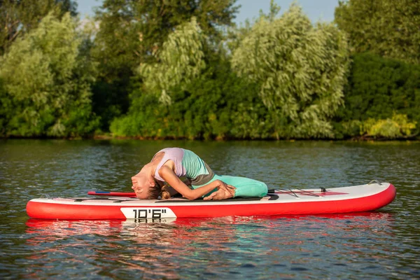 Junge Frau beim Yoga auf einem Brett mit Paddel. Yoga-Pose, Seitenansicht - Konzept der Harmonie mit der Natur. — Stockfoto