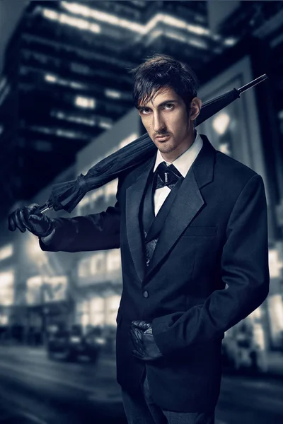 Film noir. Portrait de mode de style rétro d'un tueur. Un homme en costume avec un parapluie à la main sur un fond de ville nocturne — Photo