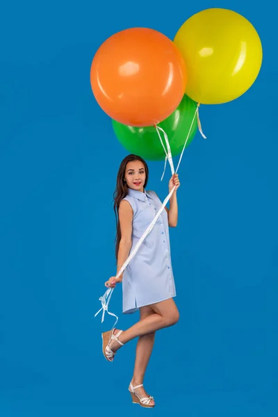 Full-length scatto di sorridente giovane donna in cerca di fotocamera e tenendo palloncini d'aria colorati isolati su blu — Foto Stock