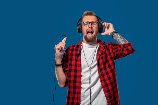 Όμορφος νέος κομψά ακουστικά κρατώντας Mp3 Player και χορό ενώ στέκεται ενάντια σε μπλε φόντο — Φωτογραφία Αρχείου