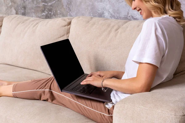 Mulher no sofá trabalhando no laptop com tela em branco mockup. Espaço de cópia vazio no monitor para propaganda. Tela preta . — Fotografia de Stock