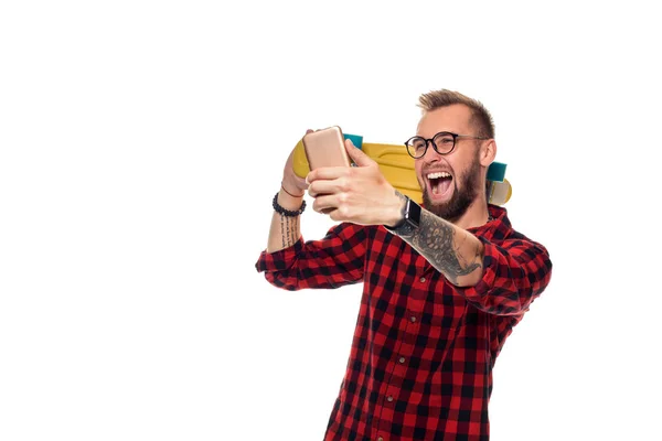Jeune homme tenant le skateboard sur l'épaule levant son téléphone prend un selfie sur un fond blanc . — Photo