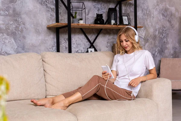 Fiatal nő zenét hallgat, miközben otthon pihen a kanapén. — Stock Fotó
