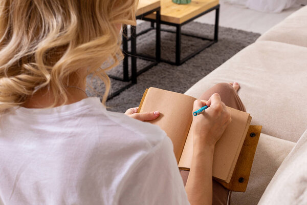 Close up woman hand writing on notebook. Young woman sitting on sofa, casual style indoor shoot