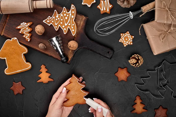 Mulher decorando biscoitos de Natal de gengibre com açúcar de confeiteiro. Conceito de preparações de Natal. Vista superior com espaço de cópia . — Fotografia de Stock