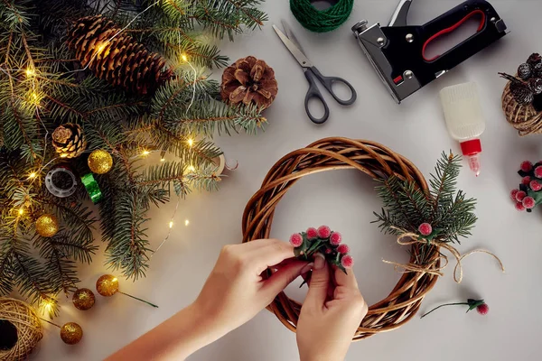 Las manos femeninas decoran la corona de Navidad con ramas de abeto con una baya roja y conos del bosque. Fondo blanco. Concepto de Año Nuevo . — Foto de Stock