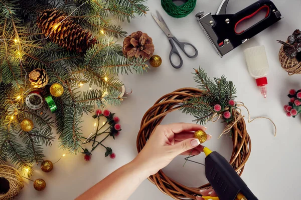 Las manos femeninas decoran la corona de Navidad con ramas de abeto con una baya roja y conos del bosque. Fondo blanco. Concepto de Año Nuevo . — Foto de Stock