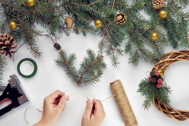 Yaratıcı Noel DIY. Kadın yapımı el yapımı Noel çelenk. Ev eğlence, Araçlar, ıvır zıvır ve Ayrıntılar için tatil dekorasyon beyaz masa arka plan üzerinde. Üstten görünüm