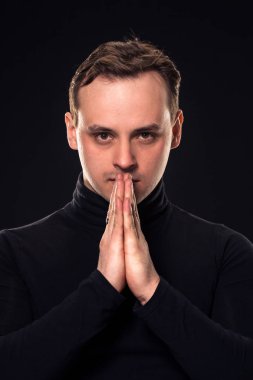 Genç adam kameraya siyah arka plan üzerinde seyir stüdyo çekim. Dikey biçimi, o ciddi bir yüz, o siyah kazak giyiyor.