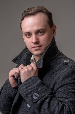 Genç adam kameraya bej renkli arka plan üzerinde seyir stüdyo çekim. Dikey biçimi, o ciddi bir yüz, gri bir ceket giyiyor.