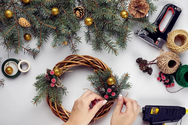 Les mains féminines décorent la couronne de Noël avec des branches d'épinette avec une baie rouge et des cônes de forêt. Fond blanc. Concept du Nouvel An . — Photo