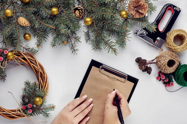 Kreativ jul diy. Kvinnan gör handgjorda xmas krans. Hem fritid, verktyg, smycken och Detaljer för julpynt på vitt bordsbakgrund. Ovanifrån — Stockfoto