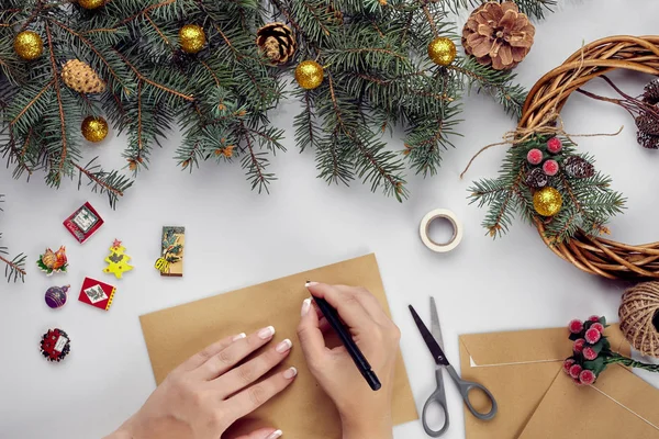 Frauenhände halten frohe Weihnachtskarte und Umschlag in der Hand. Weihnachtsdekoration Hintergrund. flache Lage, Draufsicht. — Stockfoto