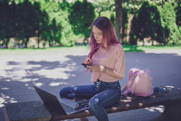 Femme écrivant dans un cahier assis sur un banc en bois dans le pair — Photo