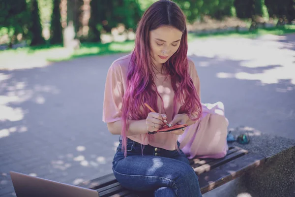 Femme écrivant dans un cahier assis sur un banc en bois dans le pair — Photo