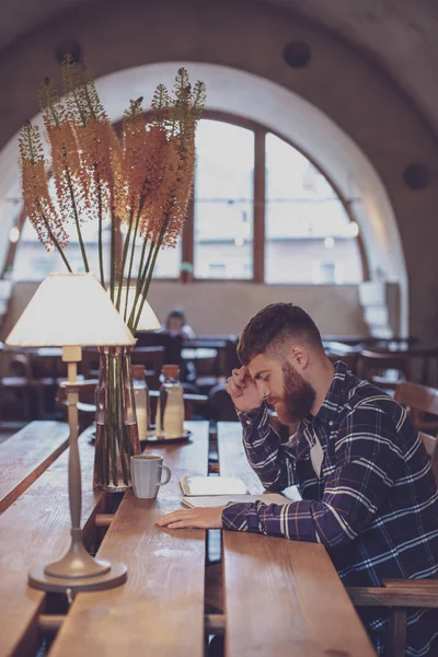 Young bearded businessman sits in cafe, home at table and writes