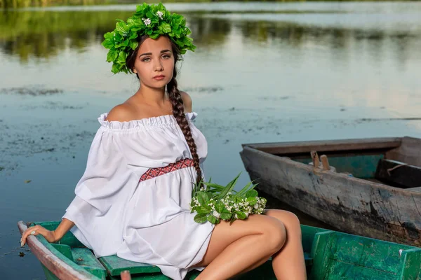 Junge sexy Frau auf einem Boot bei Sonnenuntergang. Das Mädchen trägt einen Blumenkranz auf dem Kopf, entspannt sich und segelt auf dem Fluss. Fantasy Art Fotografie. — Stockfoto
