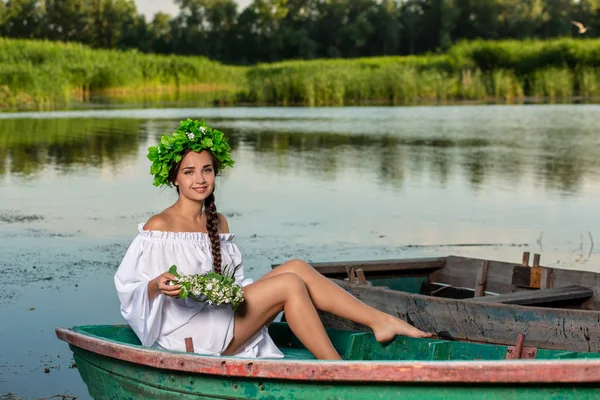 Junge sexy Frau auf einem Boot bei Sonnenuntergang. Das Mädchen trägt einen Blumenkranz auf dem Kopf, entspannt sich und segelt auf dem Fluss. Fantasy Art Fotografie. — Stockfoto
