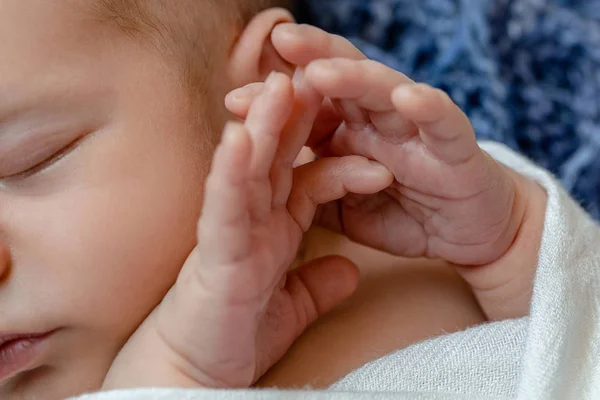 Close-up van kleine baby grepen. De slapende pasgeboren jongen onder een witte deken van gebreide ligt op de blauw bont. — Stockfoto