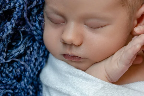 Pasgeboren baby - baby, gezicht close-up. De slapende pasgeboren jongen onder een witte deken van gebreide ligt op de blauw bont. — Stockfoto