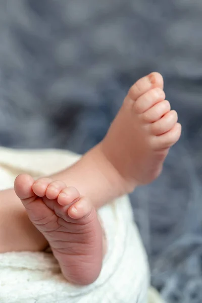 Close-up van kleine baby benen. De slapende pasgeboren jongen onder een witte deken van gebreide ligt op de blauw bont. — Stockfoto