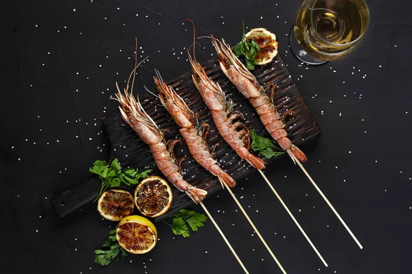 Grilled shrimp skewers. Seafood, shellfish. Shrimps Prawns skewers with herbs, garlic and lemon on black stone background, copy space.