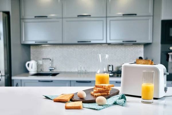 Тост зі свіжим тостом, яйцями та склянкою апельсинового соку на легкому кухонному столі — стокове фото