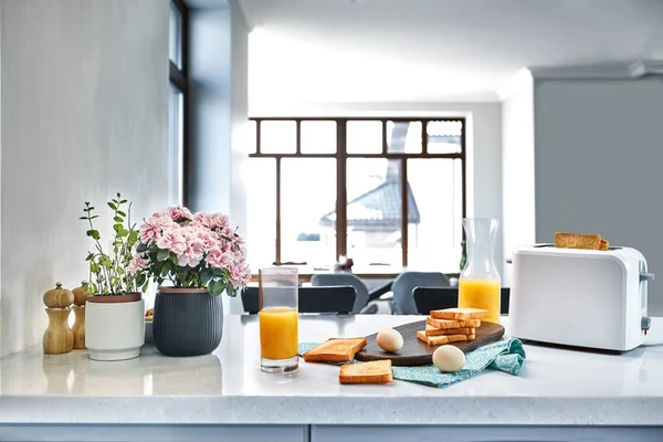 Brödrost med färskt rostat bröd, ägg och glas apelsinjuice på en ljus köksbordet — Stockfoto