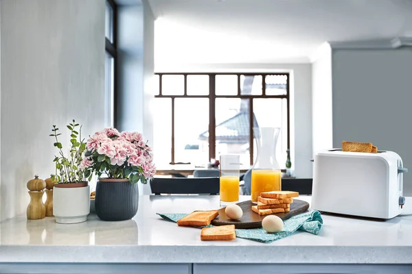 Brödrost med färskt rostat bröd, ägg och glas apelsinjuice på en ljus köksbordet — Stockfoto